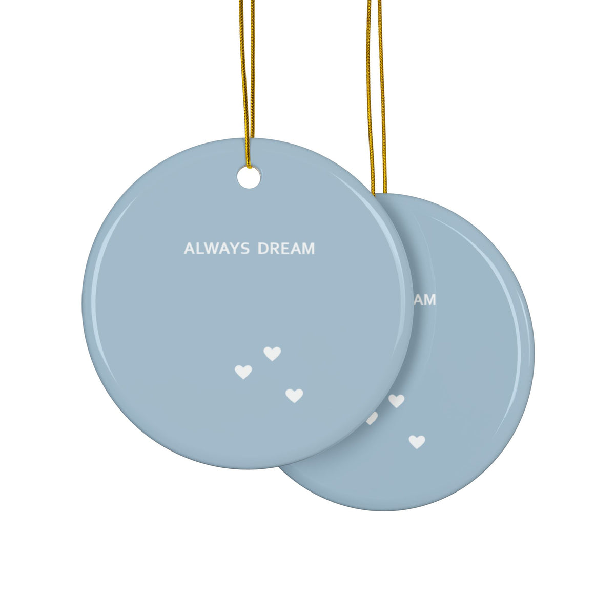 Two round light blue hanging ornaments with gold strings, one showing the front with the text 'ALWAYS DREAM' and small white hearts, and the other showing part of the back. The same text is displayed on both sides.
