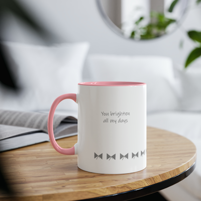 white ceramic mug with pink handle and pink inside. horizontal stripe of grey bows around bottom. the words you brighten all my days