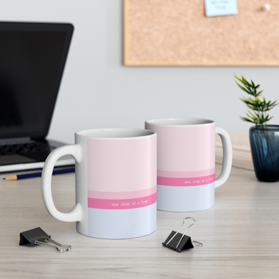 pink ceramic mug with blue and pink horizontal stripes, and the words, one step at a time.