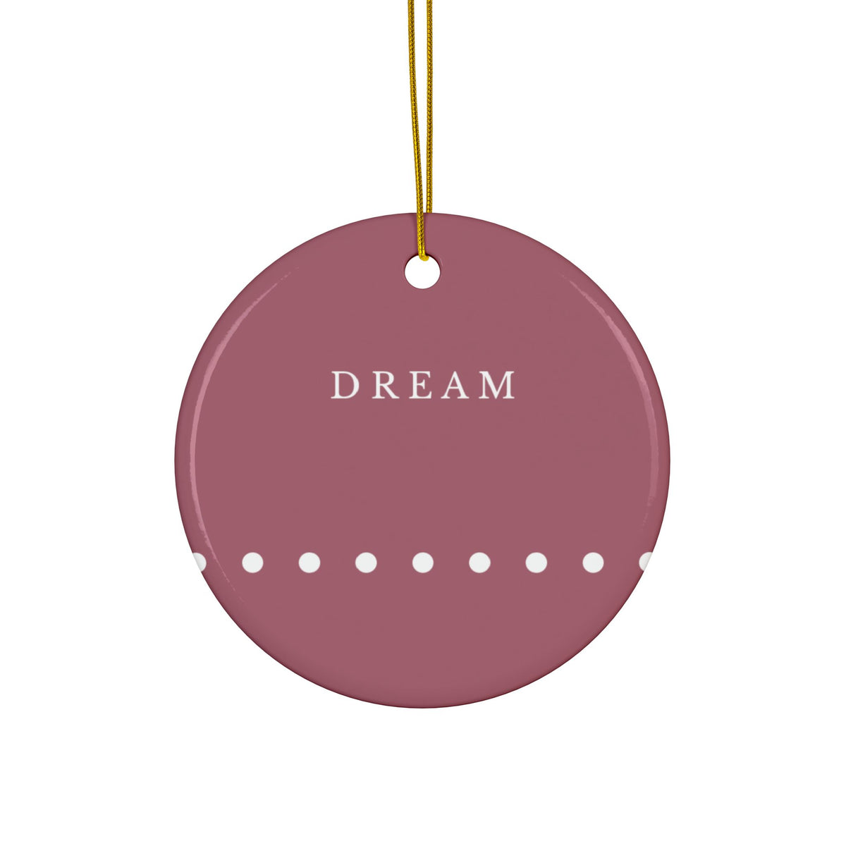 A round dark red ceramic ornament with the word 'DREAM' in white serif letters and a row of white dots along the bottom edge, hanging from a gold string against a white background.