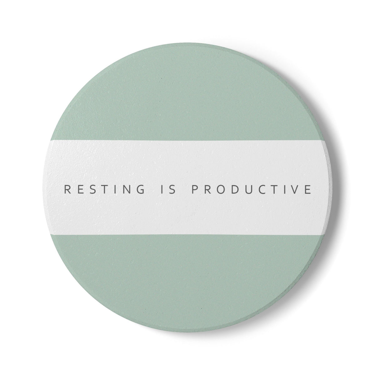 A round coaster with a minimalist design featuring a sage green top and bottom section and a white horizontal band in the middle with the text 'RESTING IS PRODUCTIVE' in a thin gray sans-serif font. The coaster is shown on a clean white background with a soft drop shadow.