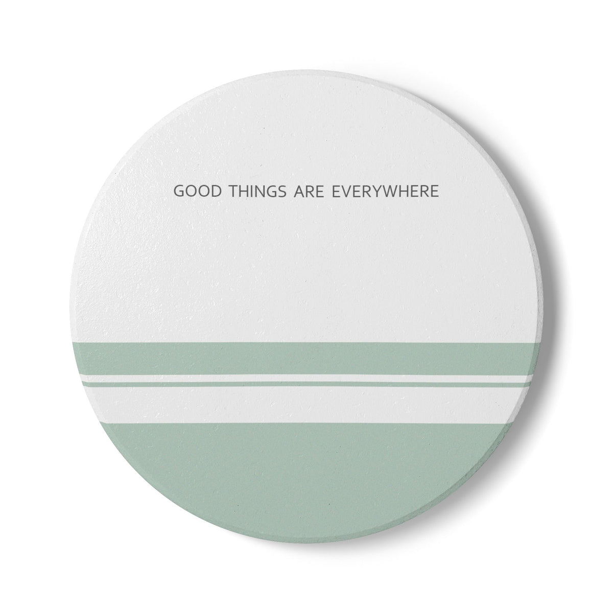 A round coaster with a minimalist design, featuring the text 'GOOD THINGS ARE EVERYWHERE' in black at the top, a white upper half, and a lower half split into three horizontal sage green stripes.