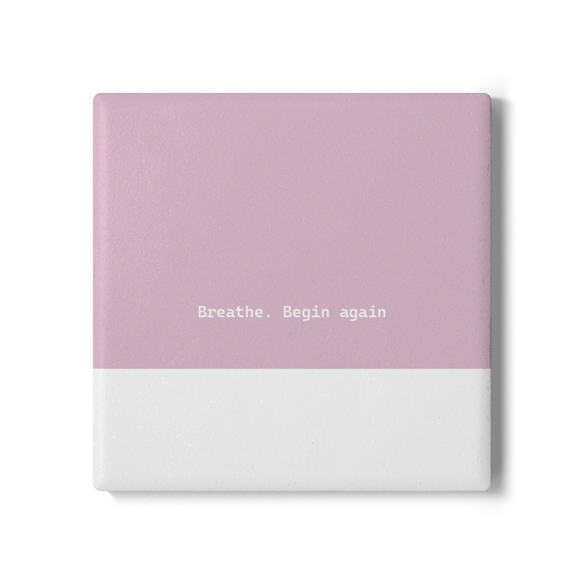 Pink and white square ceramic coaster with modern style text ‘Breathe. Begin again’ in white font. 