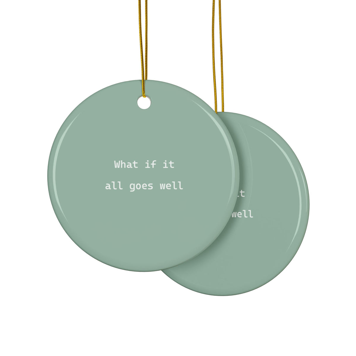 Two overlapping round hanging ornaments in sage green with white text 'What if it all goes well', suspended by gold strings on a white background.