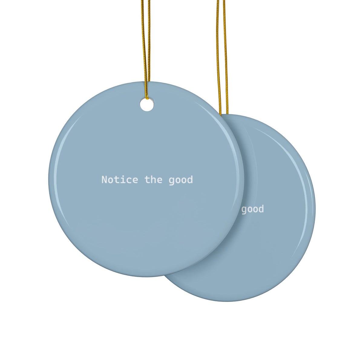 Two overlapping round hanging ornaments in blue with white text 'Notice the good', suspended by gold strings on a white background.