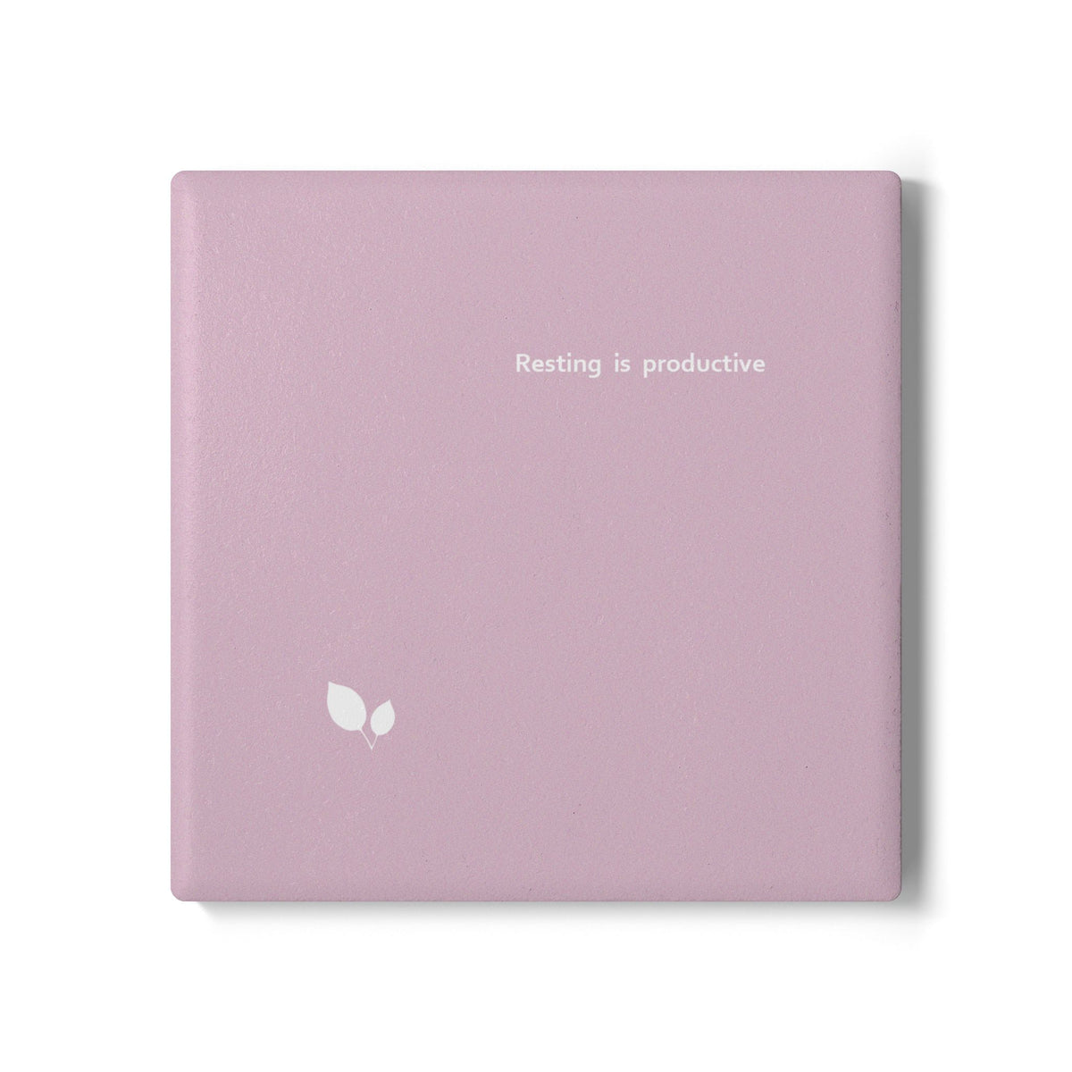 Pink square ceramic coaster with delicate leaf motif design, and small, modern style text ‘Resting is productive’ in white font.