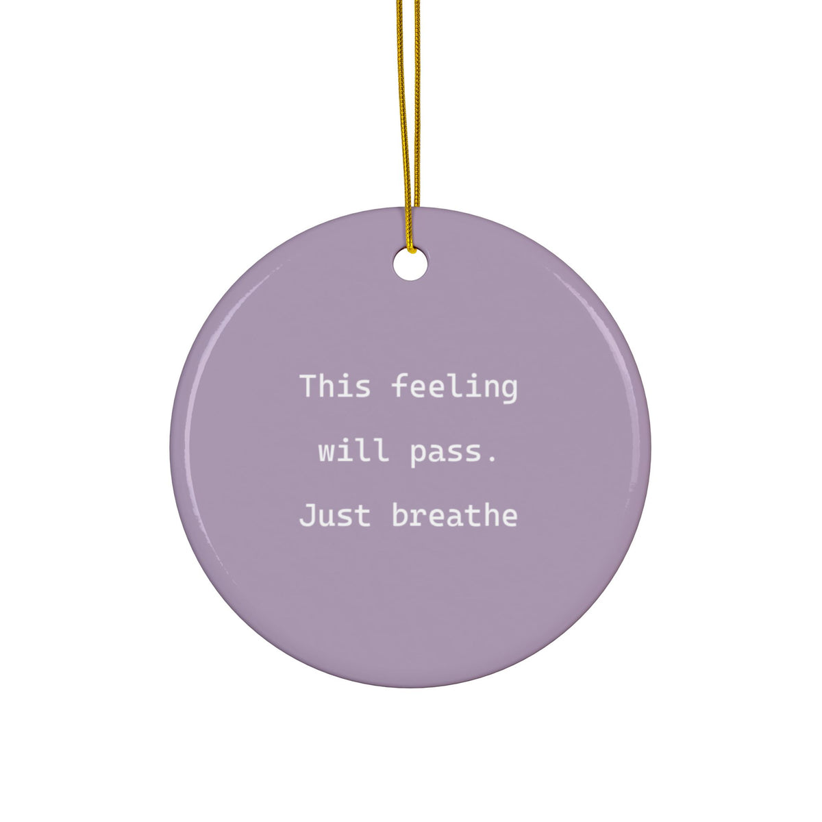 A round lavender ceramic ornament with white printed text reading 'This feeling will pass. Just breathe', hanging from a gold string against a plain white background.