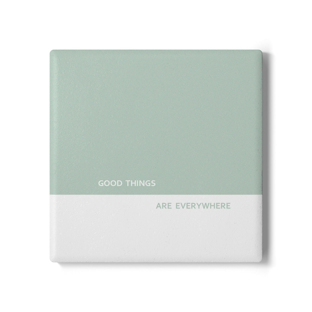 A square ceramic tile coaster with a split design, featuring a sage green top half and a white bottom half with the printed text 'GOOD THINGS ARE EVERYWHERE', shown on a white background.