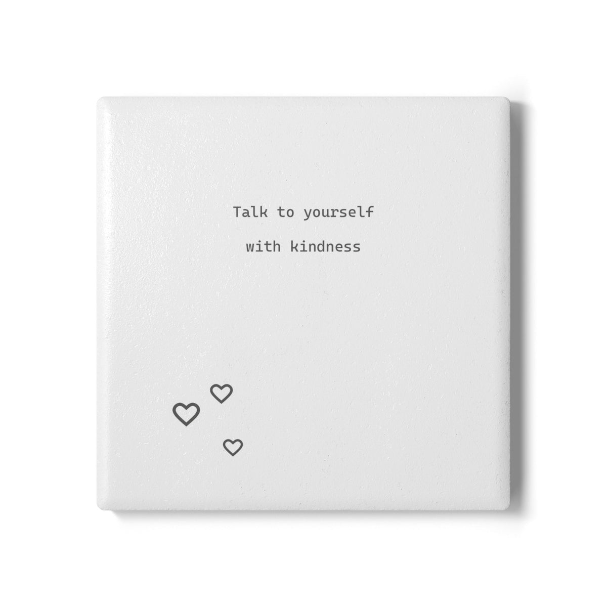 A square white coaster with the printed phrase 'Talk to yourself with kindness' in a small serif font, plus three small heart outlines near the lower left, shown on a clean white background.