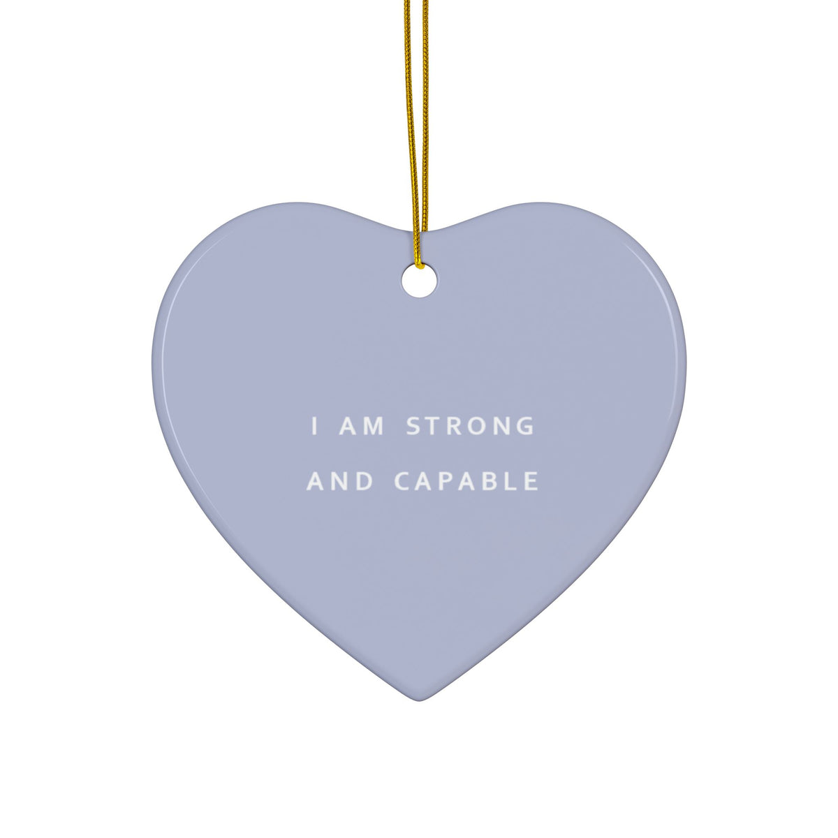 A heart-shaped ceramic ornament in a dusty lavender-lilac color with the text 'I AM STRONG AND CAPABLE' printed in white. It hangs from a gold string against a solid white background.