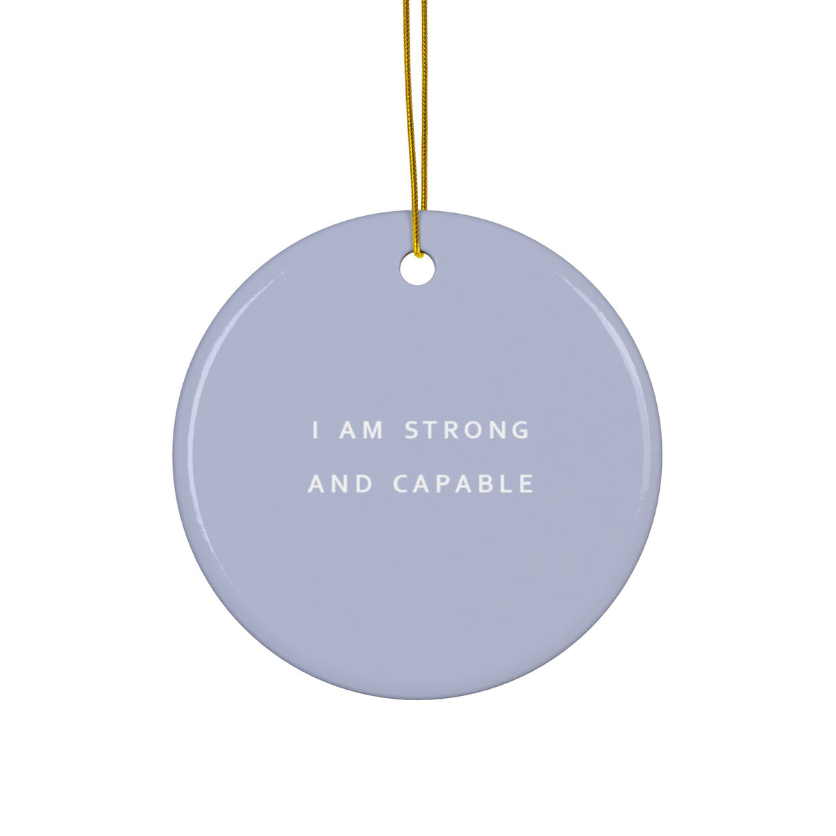A round lilac ceramic ornament with the text 'I AM STRONG AND CAPABLE' in white, hanging from a gold string against a white background.