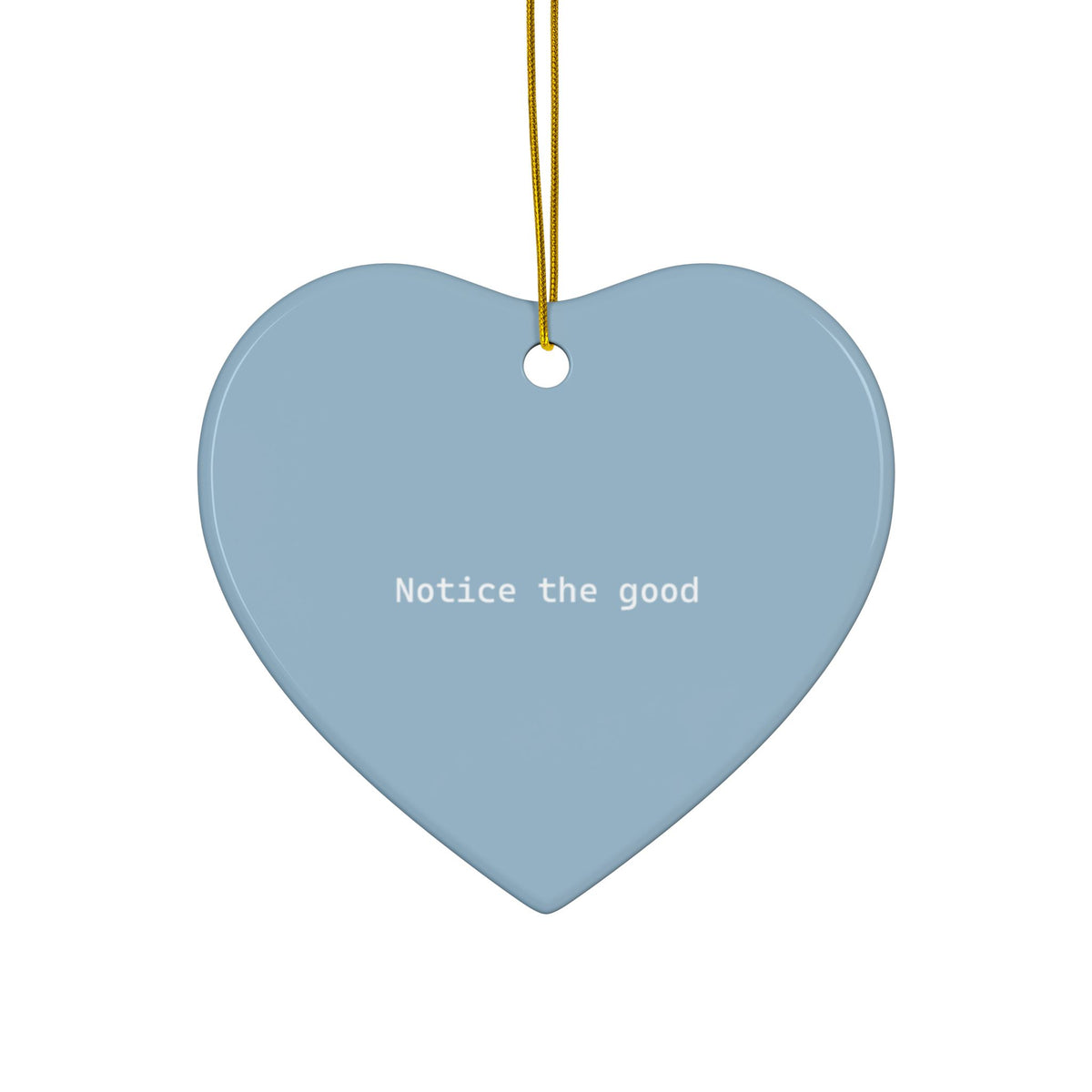 A heart-shaped light blue ceramic ornament with the phrase 'Notice the good' printed in white text, hanging from a gold string against a plain white background.