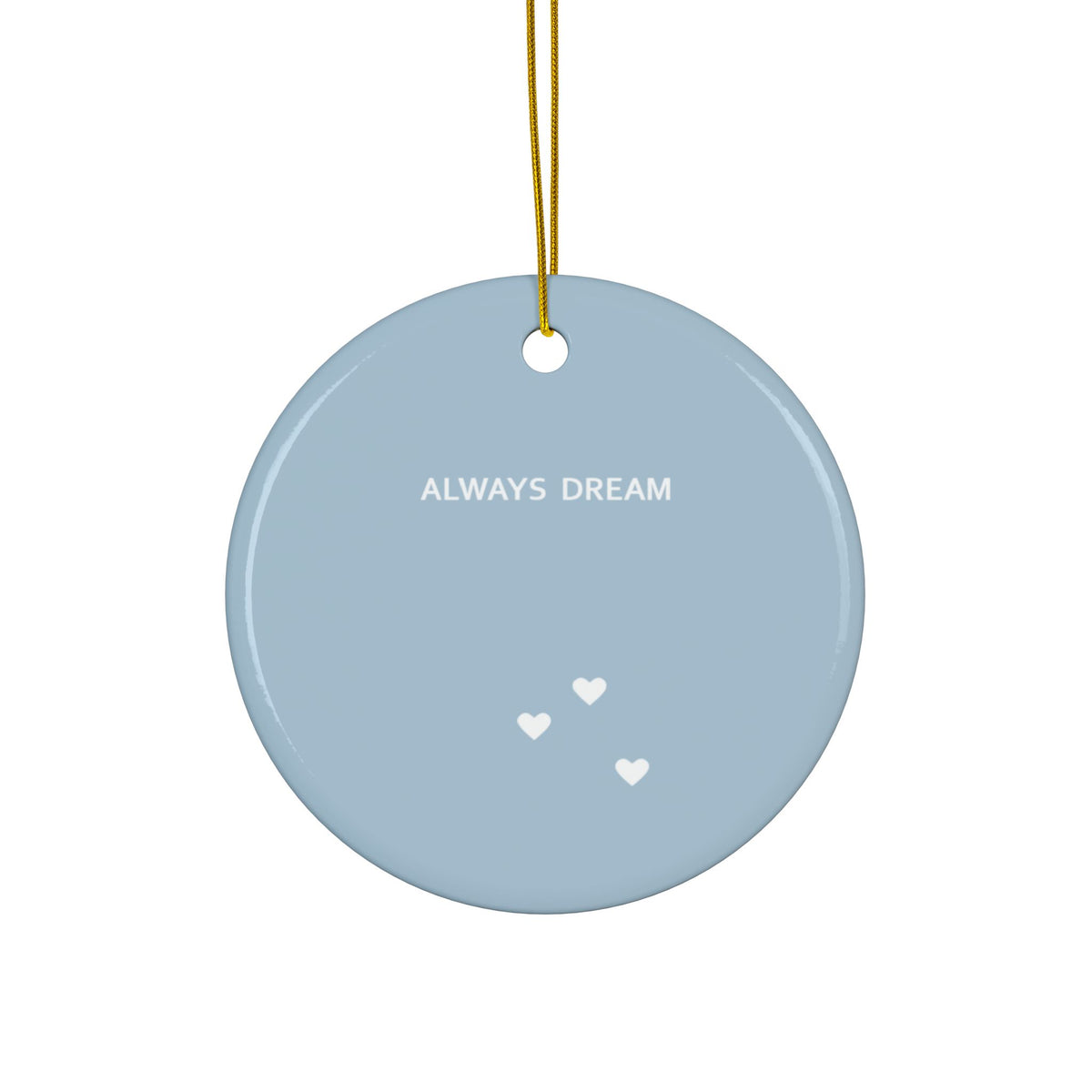 A round light blue ceramic ornament with the words 'ALWAYS DREAM' in white text and three small white hearts, hanging from a gold string on a white background.
