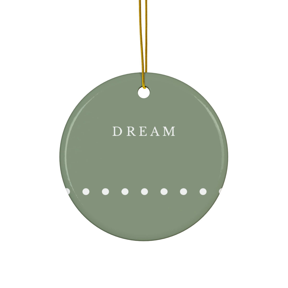 A round sage green ceramic ornament with the word 'DREAM' in white serif letters, a row of white dots along the bottom edge, and a gold hanging string at the top, shown against a plain white background.