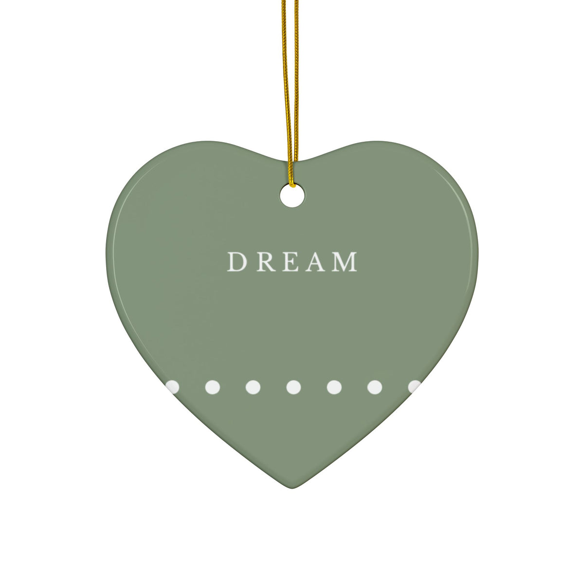 A heart-shaped ceramic ornament in sage green with the word 'DREAM' printed in white serif letters, a row of white dots along the bottom edge, and a gold hanging string at the top, shown on a plain white background.