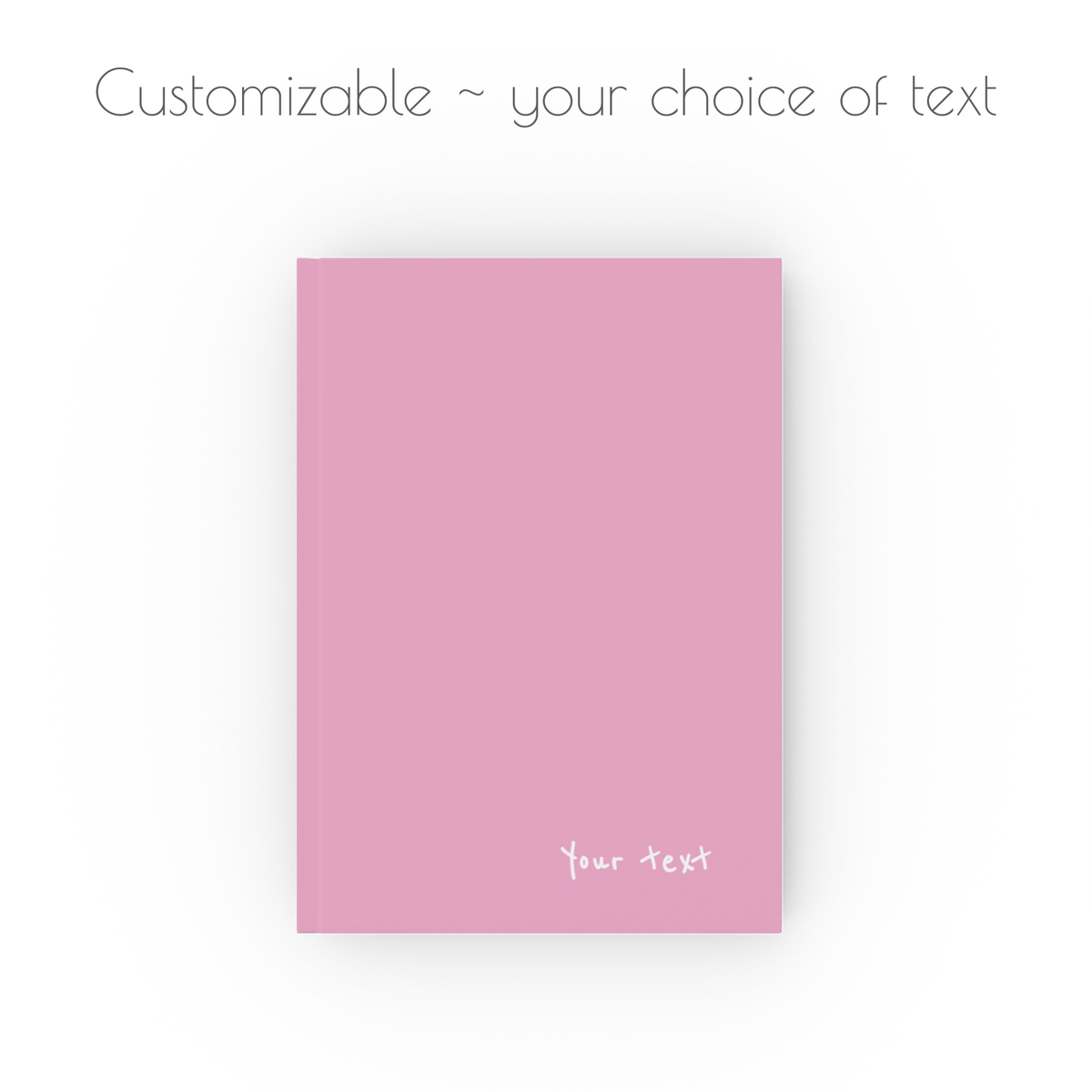 A pink, hardcover, a5 journal notebook with white handwritten style text that is customizable with your choice of personalized text.