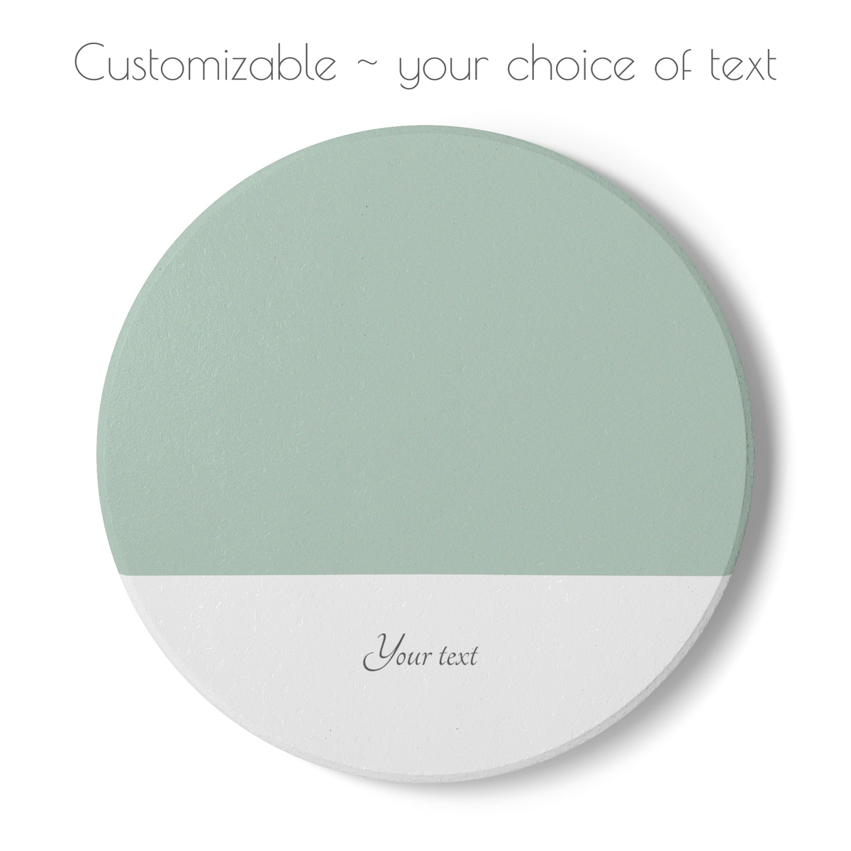 A round customizable coaster shown on a white background, with a sage green top half and a white bottom half. Placeholder text reads 'Your text' on the lower section, and additional text at the top says 'Customizable ~ your choice of text'.