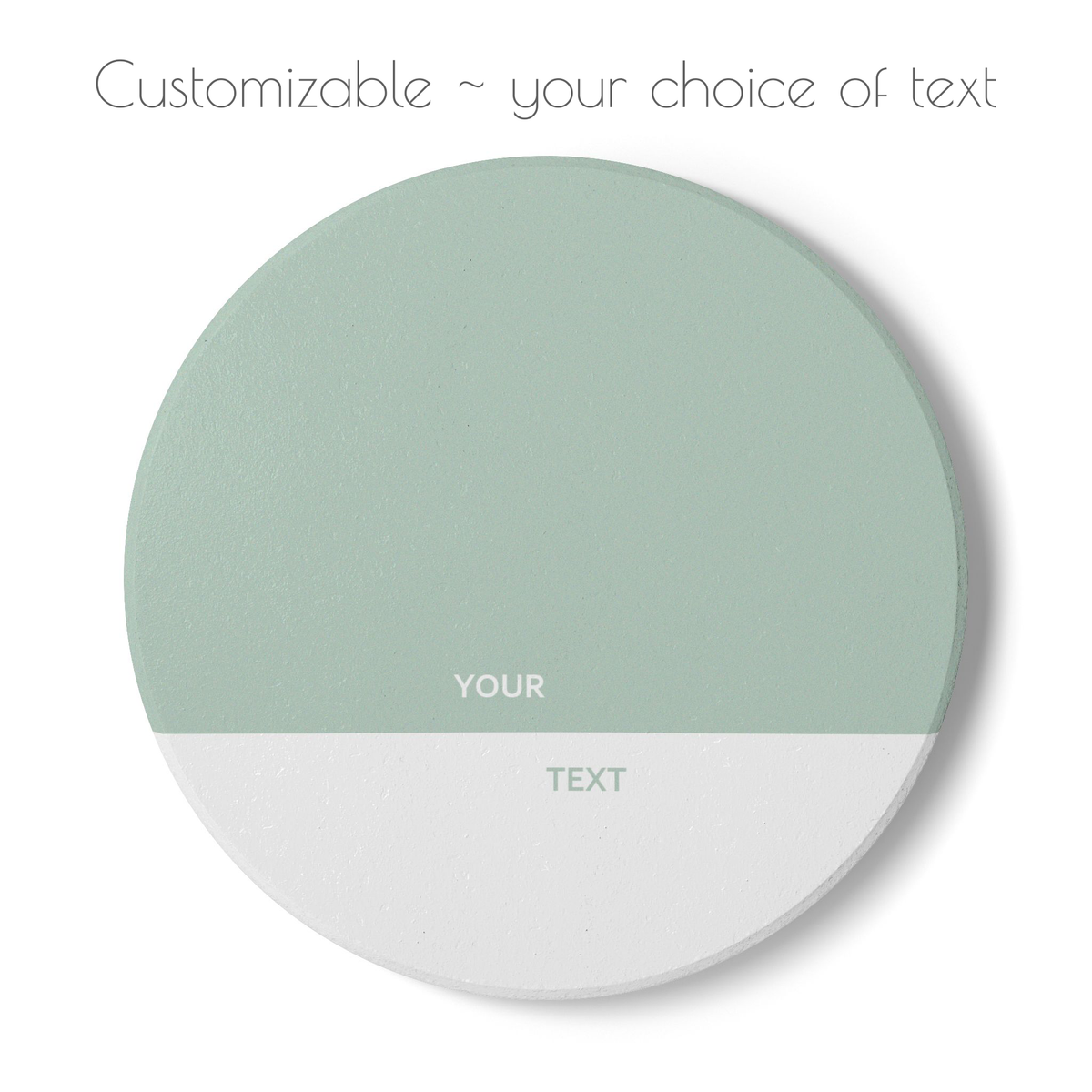 A round customizable coaster shown on a white background with the text 'Customizable ~ your choice of text' above it. The coaster is split horizontally into two sections: a sage green top half labeled 'YOUR' and a white bottom half labeled 'TEXT'.