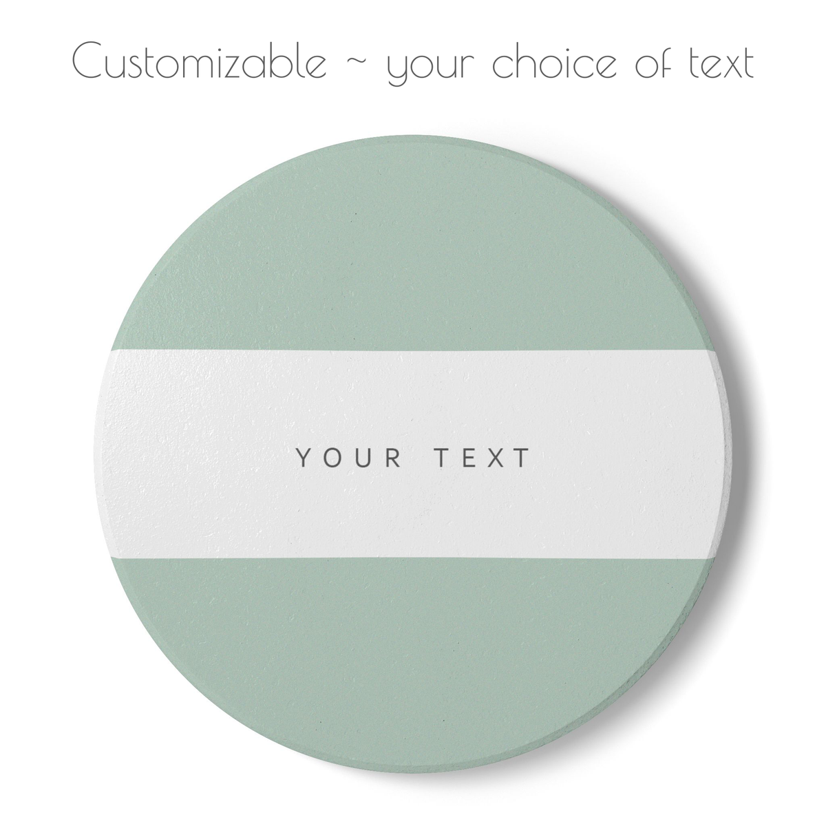 A round customizable coaster with a horizontal white stripe across the center, flanked by muted sage green sections. The center features the placeholder text 'YOUR TEXT' in a thin black font.