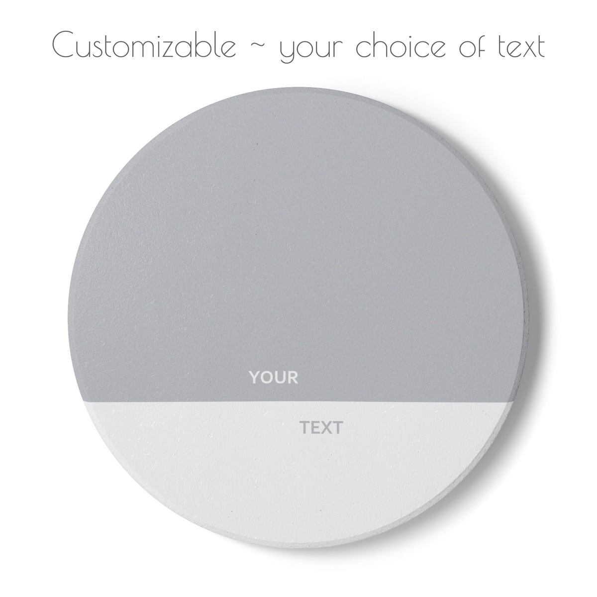 A round customizable ceramic coaster with a two-tone design, featuring a medium gray top half and a white bottom half with placeholder text 'YOUR' and 'TEXT'. The top of the image includes the text 'Customizable ~ your choice of text' on a plain white background.