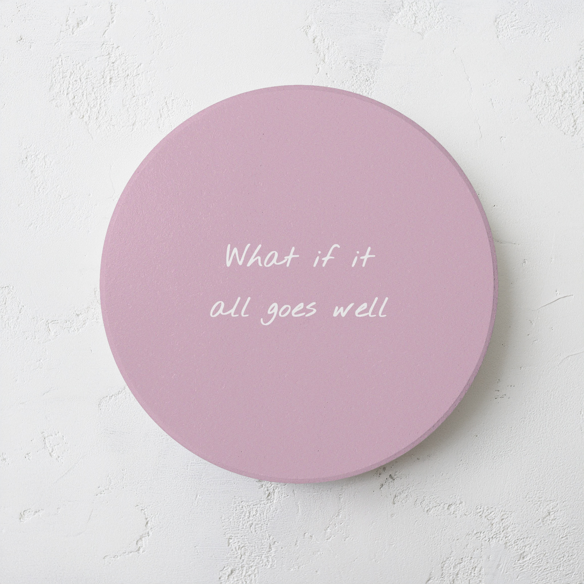 Pink round ceramic coaster with handwritten style text ‘What if it all goes well’ in white font. The coaster is on a grey cement style surface.