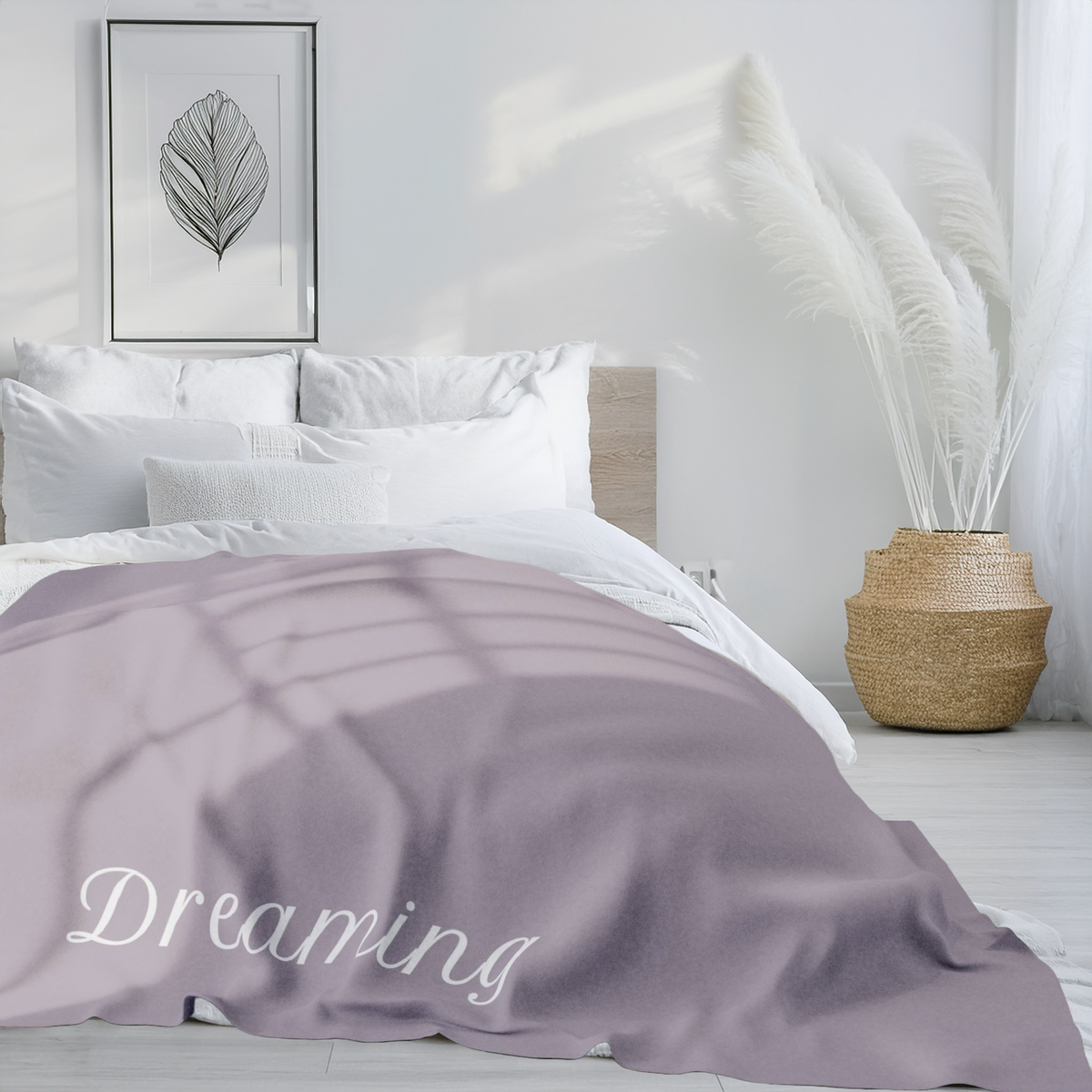 Taupe brown blanket with large, elegant font in white for the text ‘Dreaming'.  The blanket is on a bed in a modern bedroom with large vase and contemporary artwork on the wall