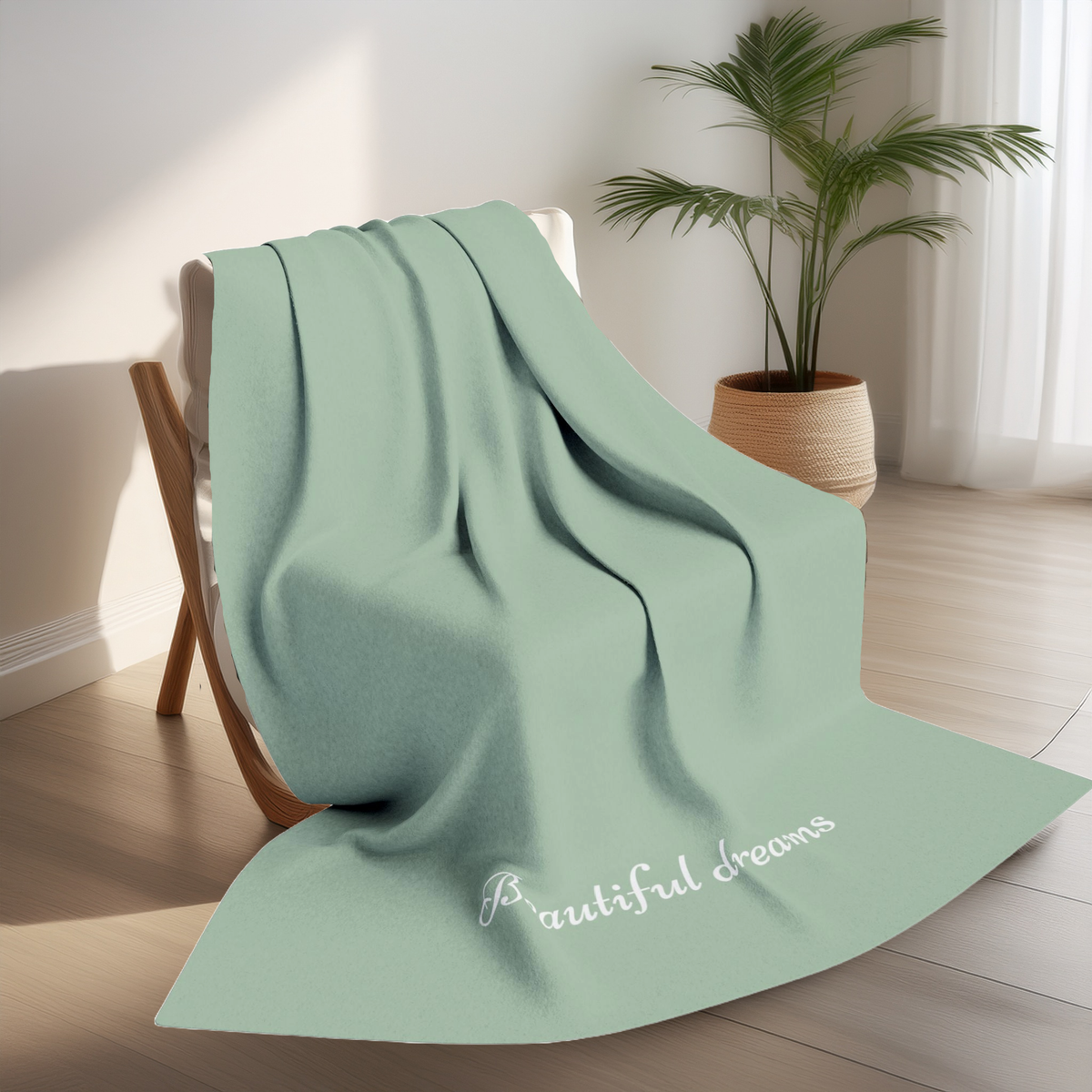 Green blanket with elegant font in white for the text ‘Beautiful dreams’ along the bottom.  The blanket is on a chair in a living room with plant in the background.