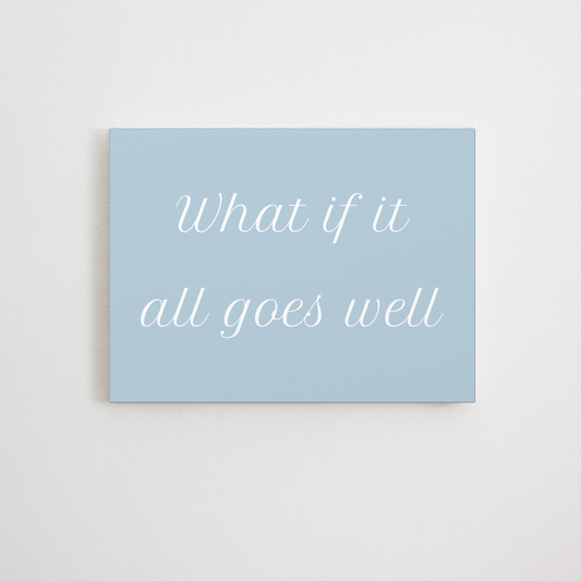 A canvas wall art print with the phrase 'What if it all goes well' in white cursive text on a light blue background, displayed against a neutral off-white wall.