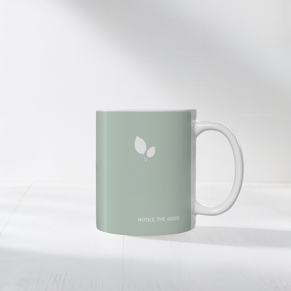 11oz green ceramic mug with small white leaf cluster design. Small white font at the bottom ‘Notice the good’. The mug sits on a white surface, minimalist background.