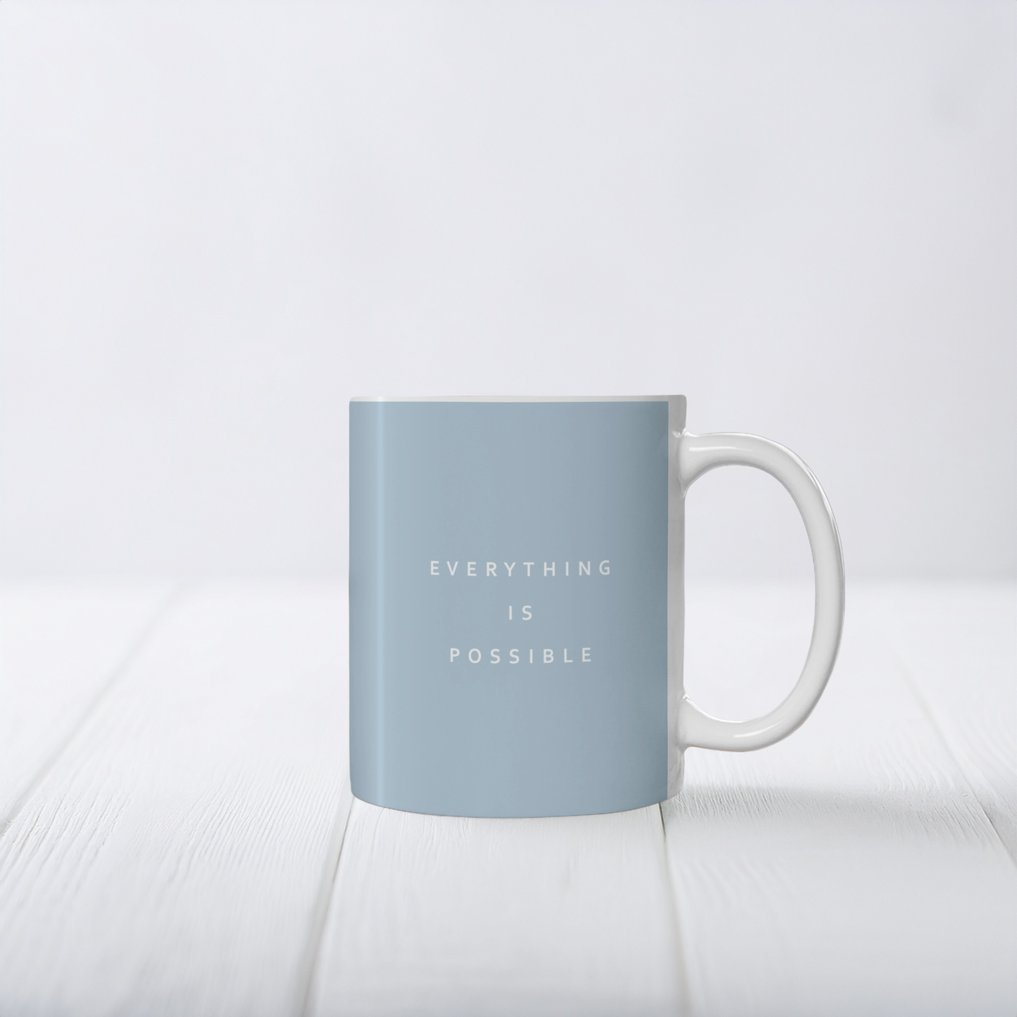11oz blue ceramic minimalist mug. Small white font in the middle ‘Everything is possible’.  The mug sits on a white surface, minimalist background.