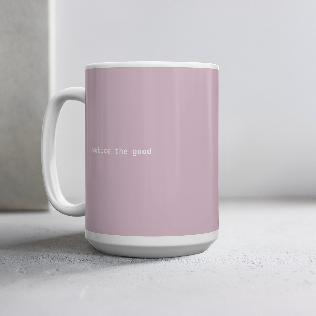 Light pink ceramic mug with small white font in the middle ‘Notice the good'. The 15oz mug sits on a cement style surface, minimalist background.