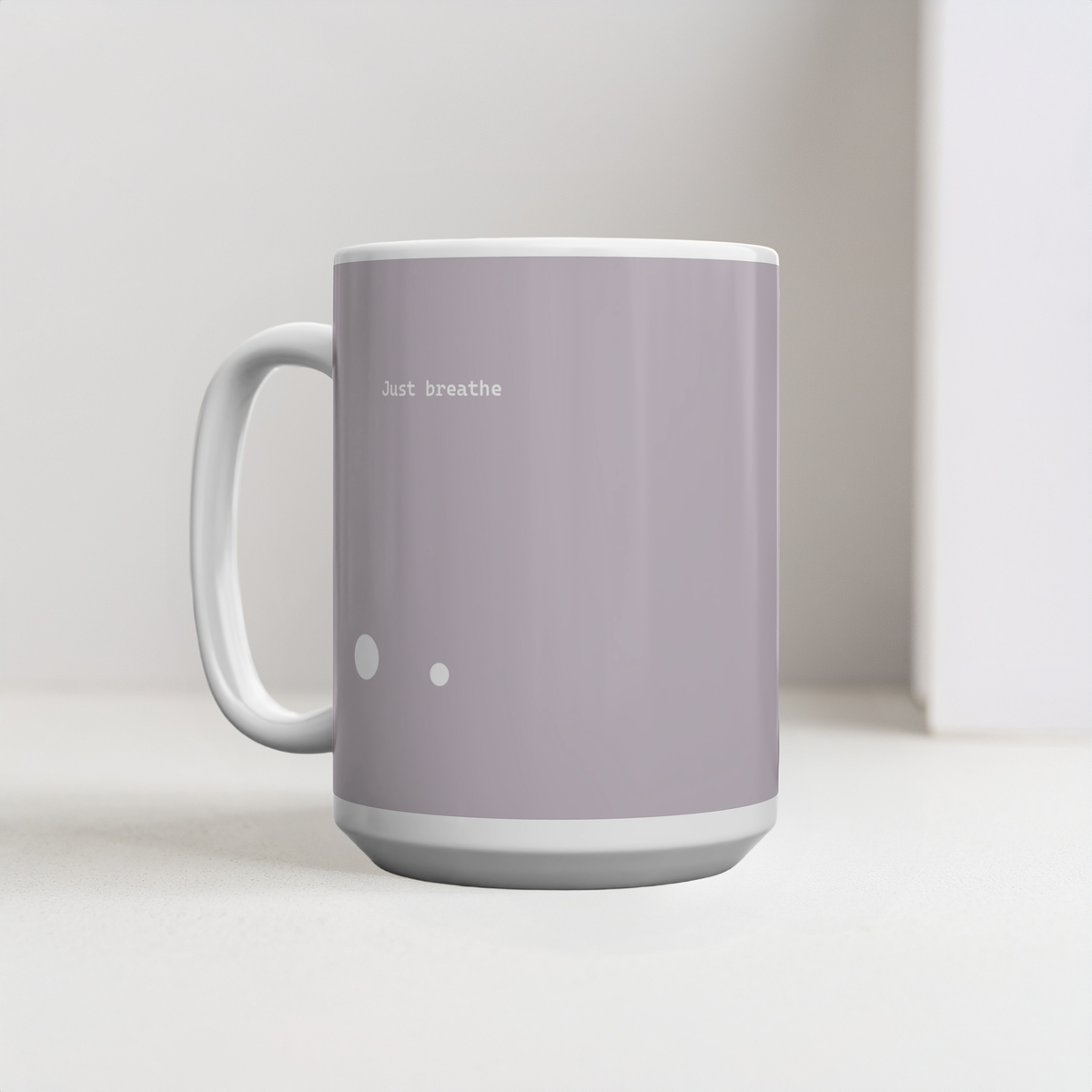 Taupe brown ceramic mug with two small white circle dots design. Small white font at the top ‘Just breathe’. The 15oz mug sits on a white surface, minimalist background.