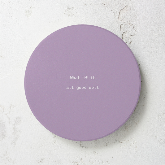 Purple round ceramic coaster with modern style text ‘What if it all goes well’ in white font. The coaster is on a  cement style surface.