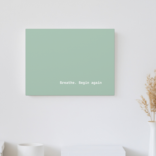 A minimalist wall art canvas print in a muted sage green color, featuring the white typewriter-style text 'Breathe. Begin again.
