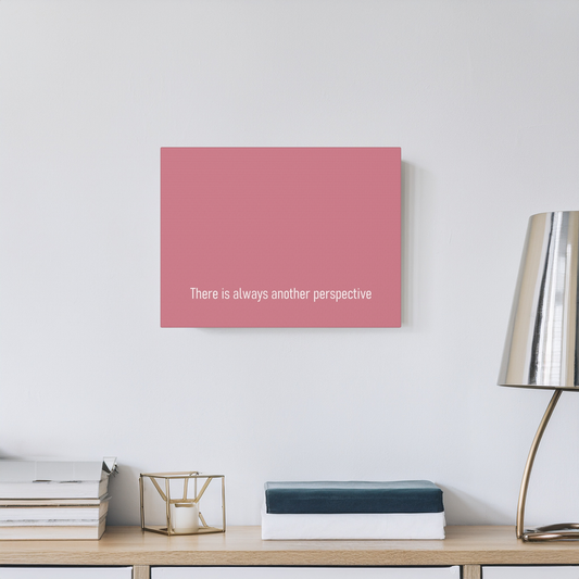 A red rectangular wall art canvas print with the white text 'There is always another perspective' displayed on a light gray wall above a wooden console table with books and a lamp.