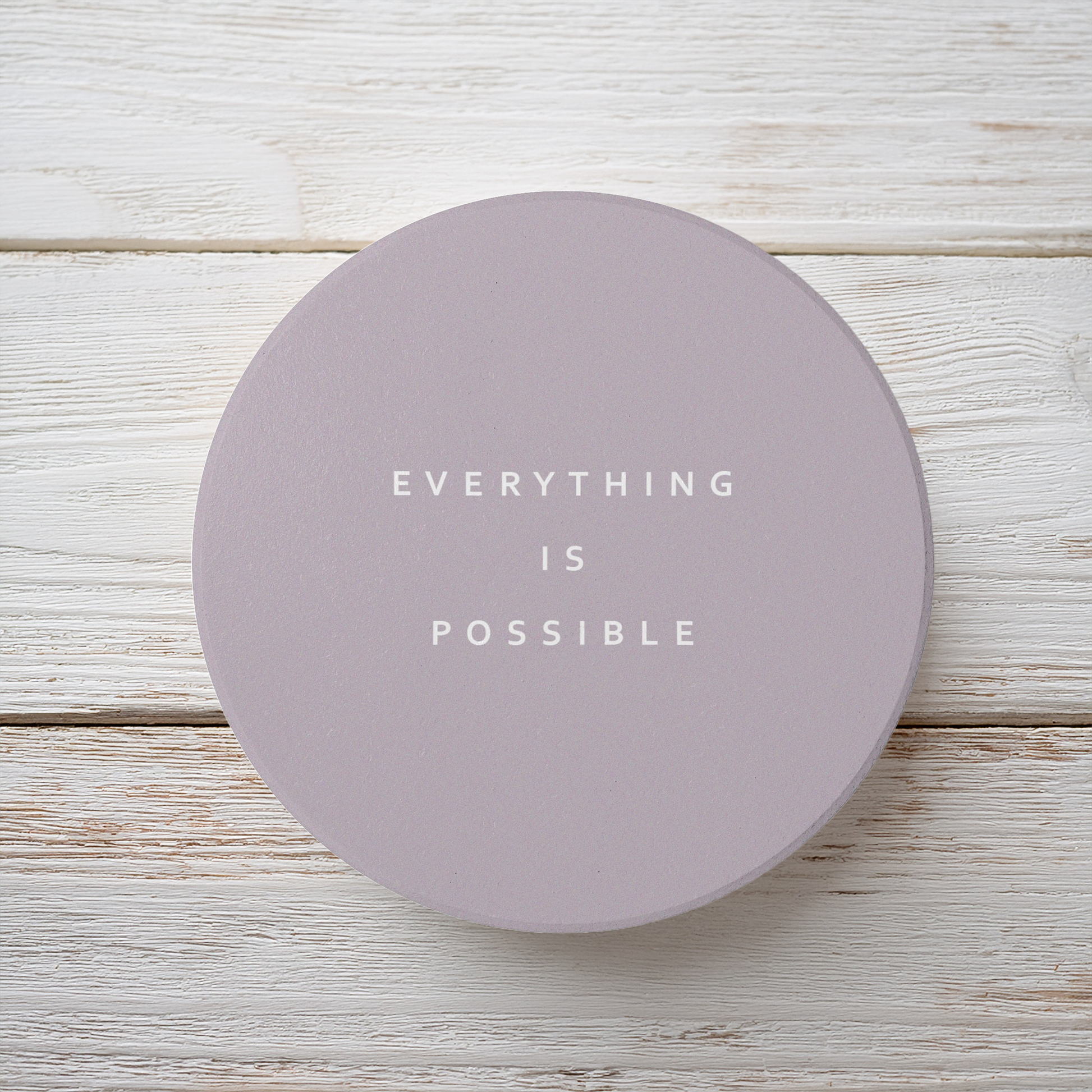 Brown round ceramic coaster with modern style text ‘Everything is possible’ in white font. The coaster is on a brown wooden surface.