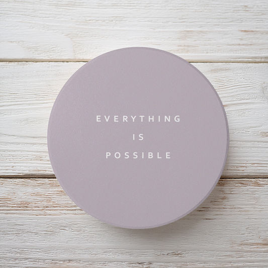 Brown round ceramic coaster with modern style text ‘Everything is possible’ in white font. The coaster is on a brown wooden surface.